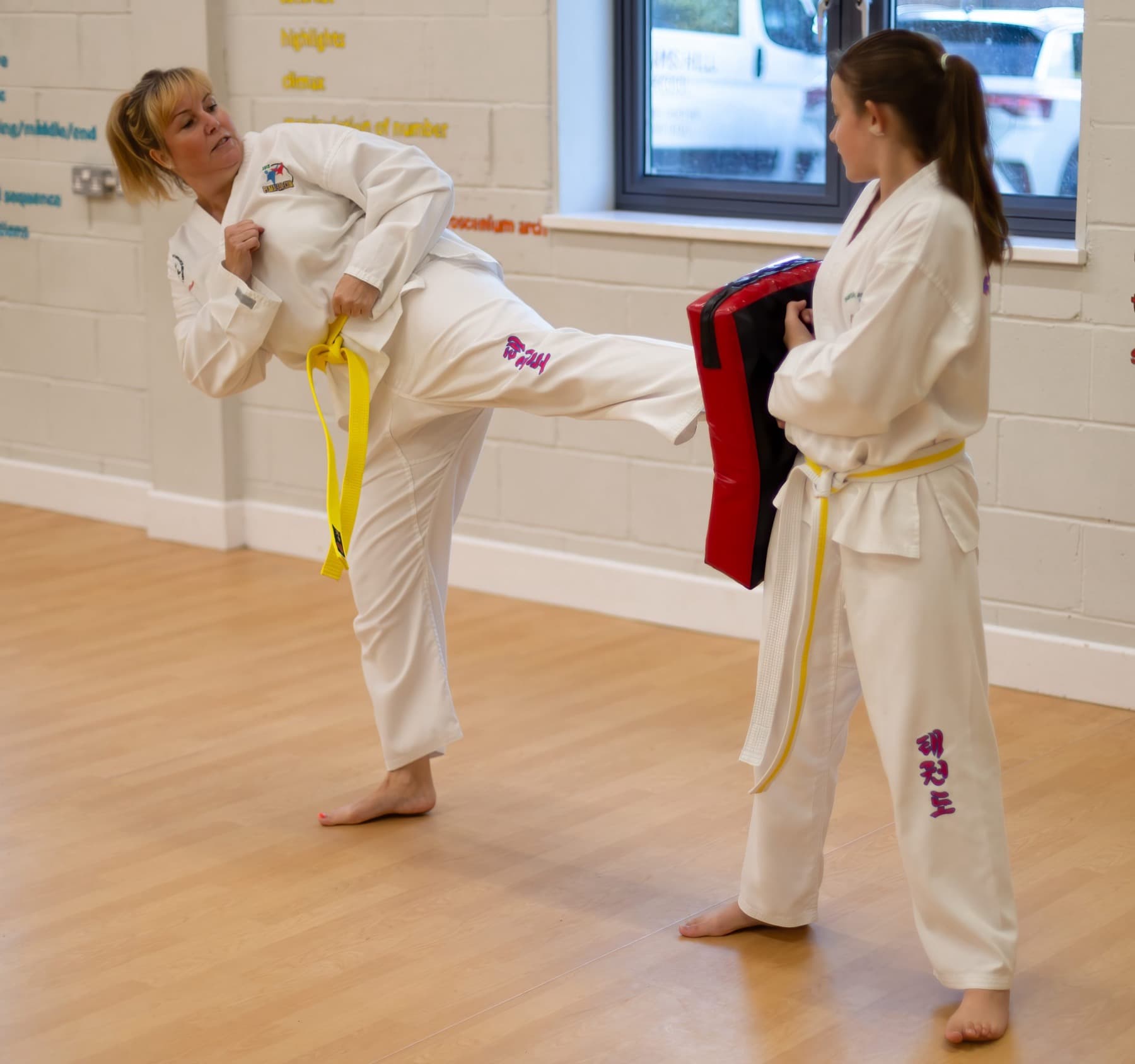 A parent and daughter practising a kick on a pad