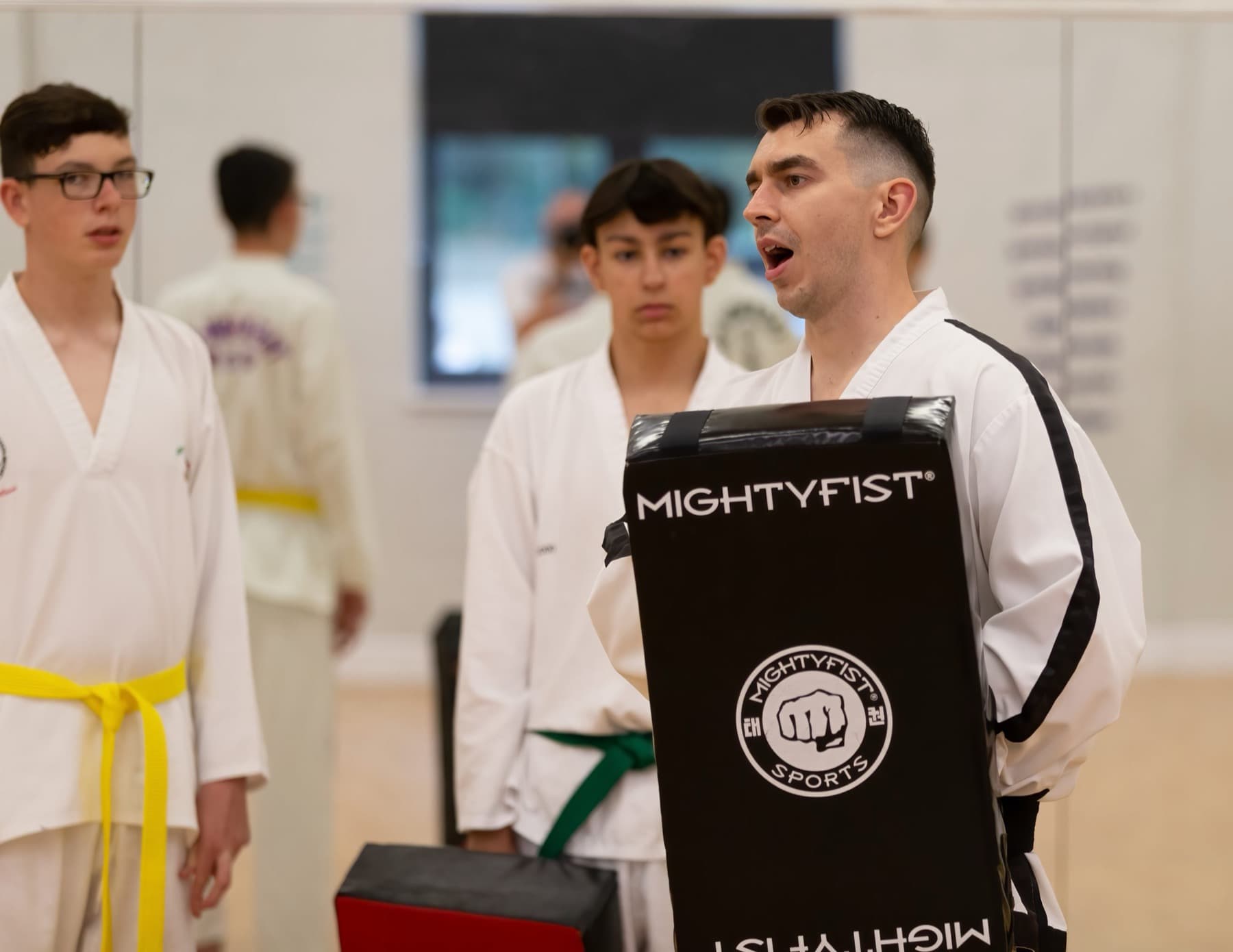 Teen and adult students with an instructor holding a kick shield